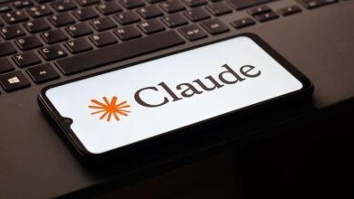 شعار كلود (Claude) على هاتف ذكي، كتبت كلمة كلود باللغة الإنجليزية بلون أسود بجانبه النجمة المشعة أو شرارة الأفكار بلون برتقالي على خلفية بيضاء على هاتف ذكي موضوع على كيبورد (لوحة مفاتيح) لونها أسود.