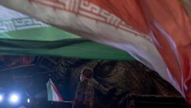 تلميذ إيراني يرتدي زي "الحرس الثوري الإيراني" يلوّح بالعلم الوطني أثناء وقوفه أمام لوحة إعلانية مناهضة للولايات المتحدة، وذلك خلال مسيرة ليلية مؤيدة للحكومة في وسط طهران، إيران، في 30 أغسطس/آب 2026.