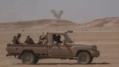 آلية عسكرية محملة بجنود القوات الحكومية اليمنية المدعومة من السعودية ويظهر في الخلف دخان قصف في أرض صحراوية