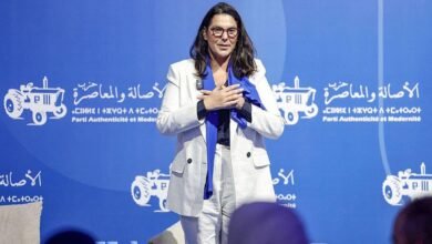فاطمة الزهراء المنصوري، منسقة القيادة الجماعية لحزب الأصالة والمعاصرة، ترتدي سترة بيضاء وبنطالا أبيض ووشاحا أزرق، وتتحدث إلى مؤيدي حزبها، وفي الخلفية لافتة كبيرة تحمل اسم الحزب ورمزه الانتخابي.