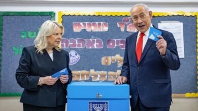 رئيس الحكومة الإسرائيلي بنيامين نتنياهو وزوجته سارة نتنياهو خلال الإدلاء بصوته في القدس في 27 أكتوبر/تشرين الثاني 2026 - يمسكان بمغلفات زرقاء ويقفان بجانب صندوق اقتراع أزرق اللون.